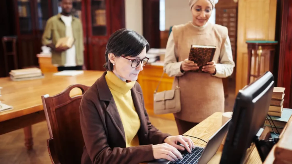 Portrait of female librarian using laptop while helping students in college library
