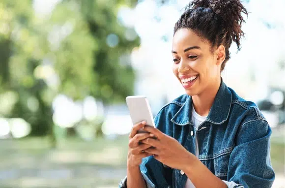 Jeune femme souriante utilisant une application de thérapie numérique (DTx) sur son smartphone dans un parc